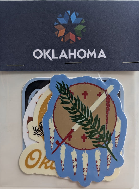 A set of die-cut stickers featuring Oklahoma-themed designs, including a prominent blue, tan, green, and red circular emblem with a bow and arrow and feathers, displayed on a white backing card with a dark blue header printed with the word 'OKLAHOMA' and a multicolor geometric logo.